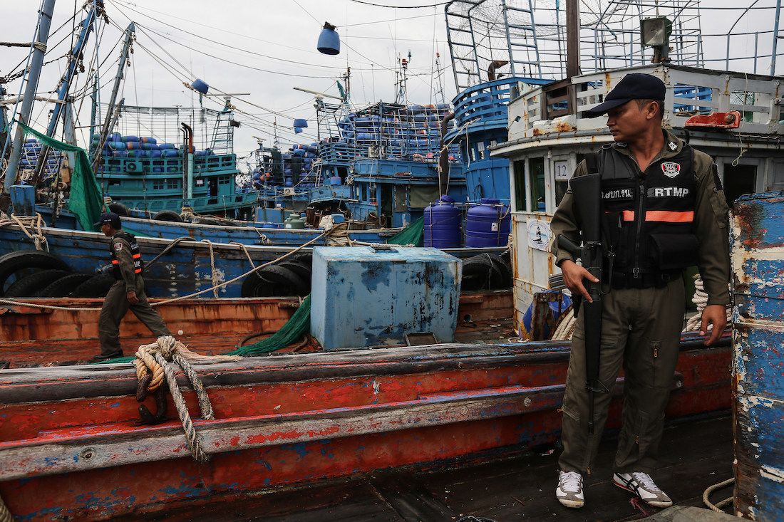 Two Thai police officers searching boats at a port.