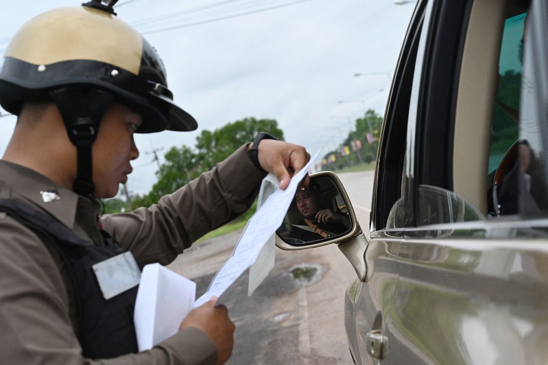A Thai policeman inspecting documents of a Laotian driver at a road checkpoint