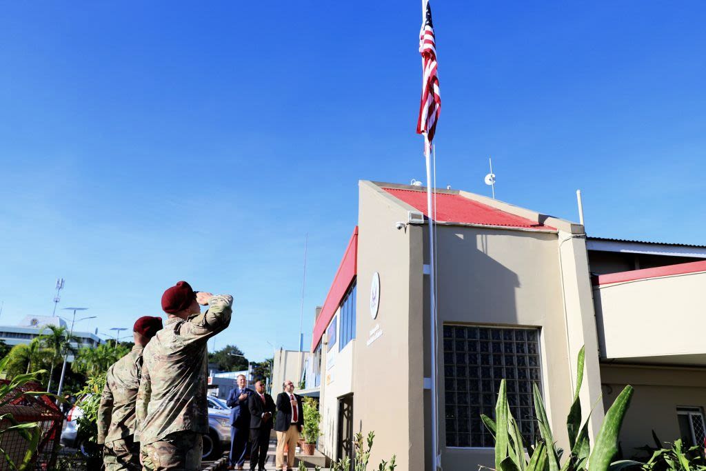 Uniformed men in berets salute a U.S. flag raising above a building.