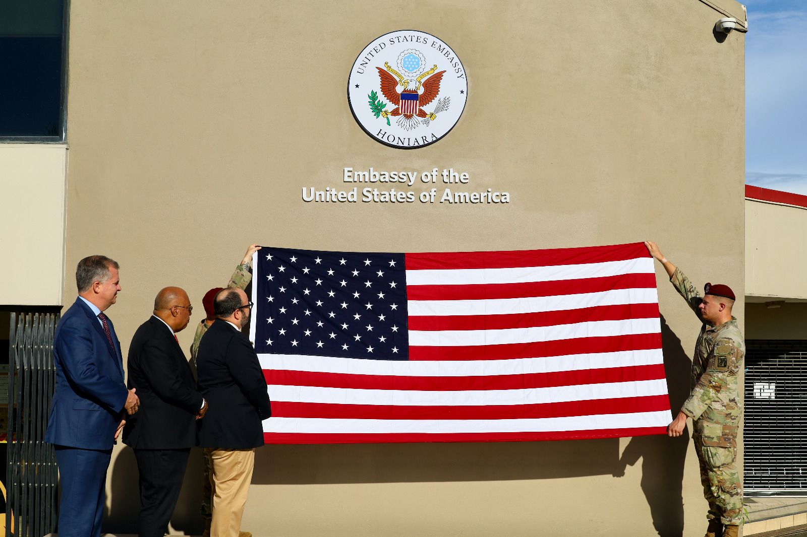Soldiers hold up a U.S. flag in front of a building that says "Embassy of the United States of America."