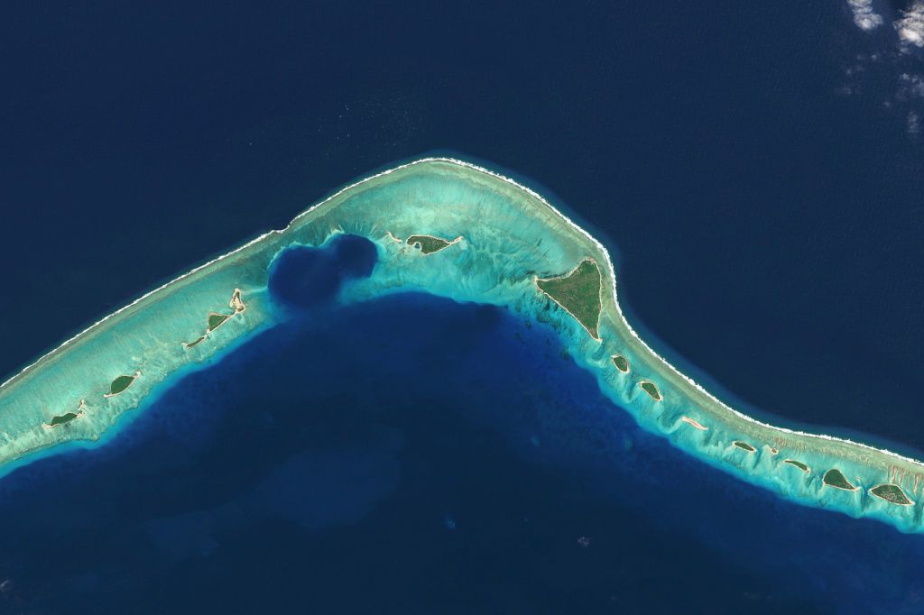 A satellite view of an island atoll with giant, gaping holes along the beach line.