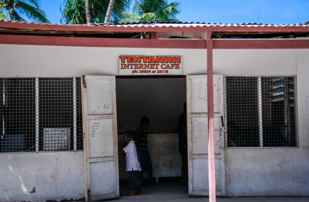 People stand in a building with a sign displayed above the entrance as an Internet Cafe.