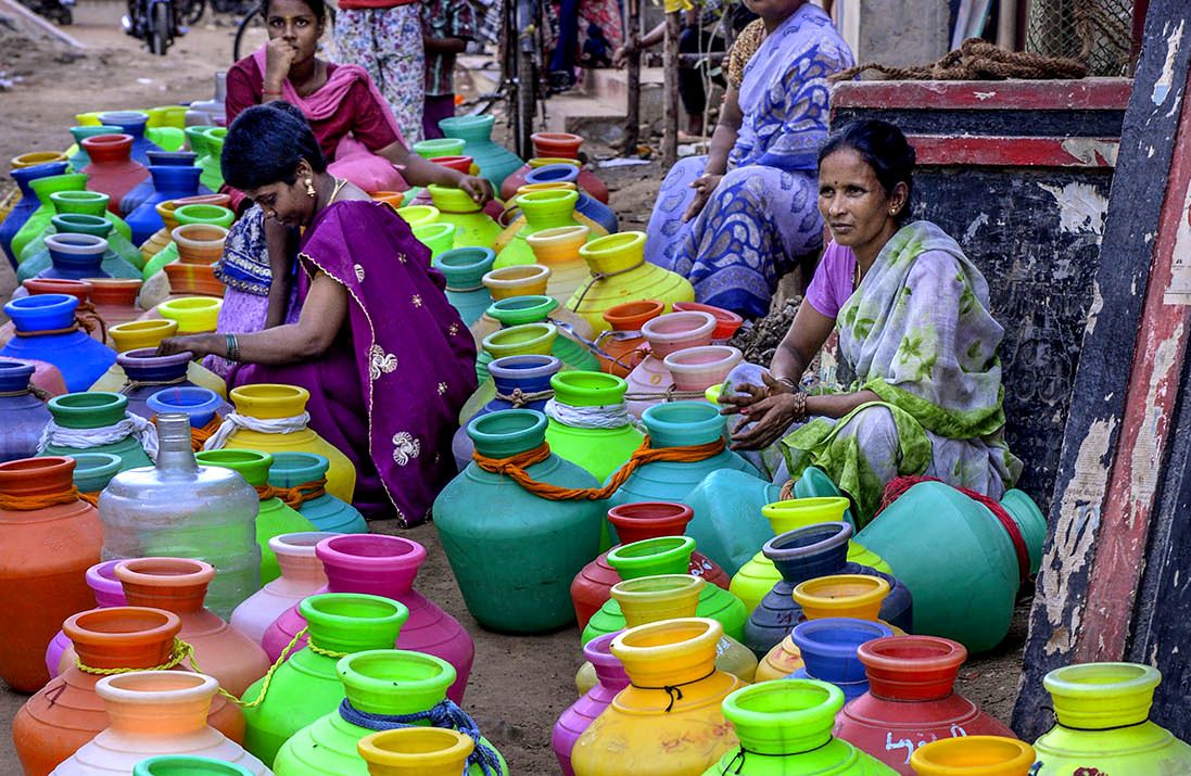 Four Indian women with multicolored jugs for water.
