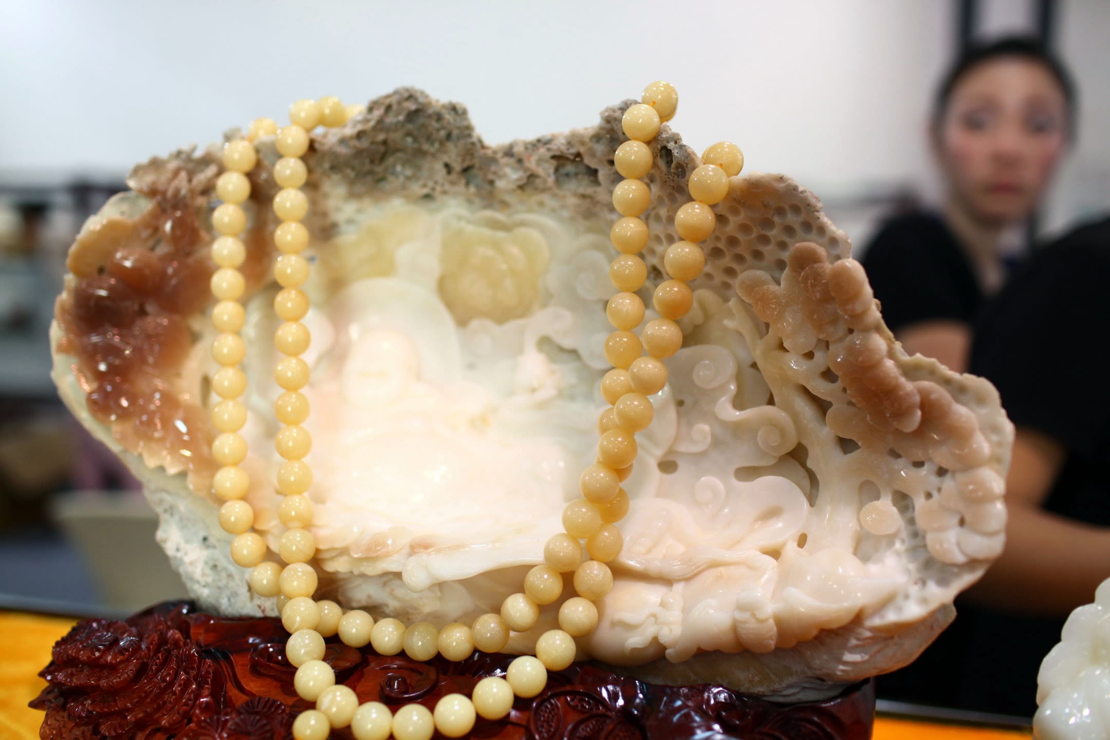 A white clamshell is carved with intricate patterns and has a string of cream-colored beads laid upon it.