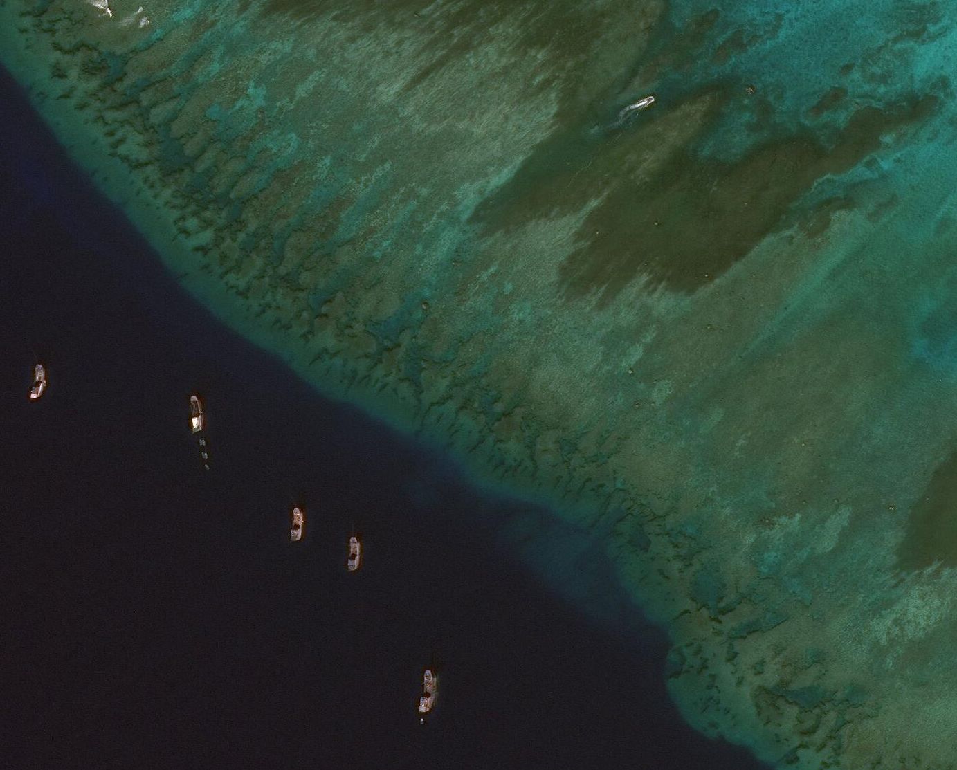 A satellite image of clam harvesting at Scarborough Shoal. Boats are shown in deep blue and green water.