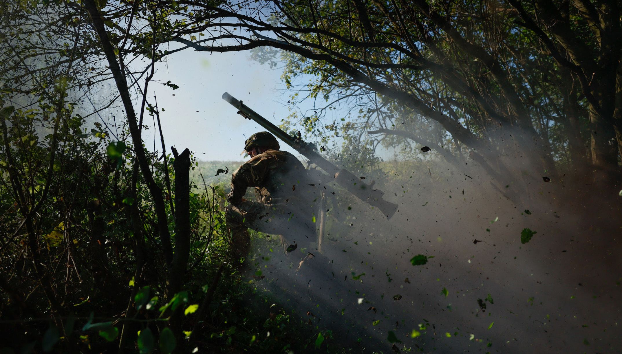 A Ukrainian soldier kneels in the brush