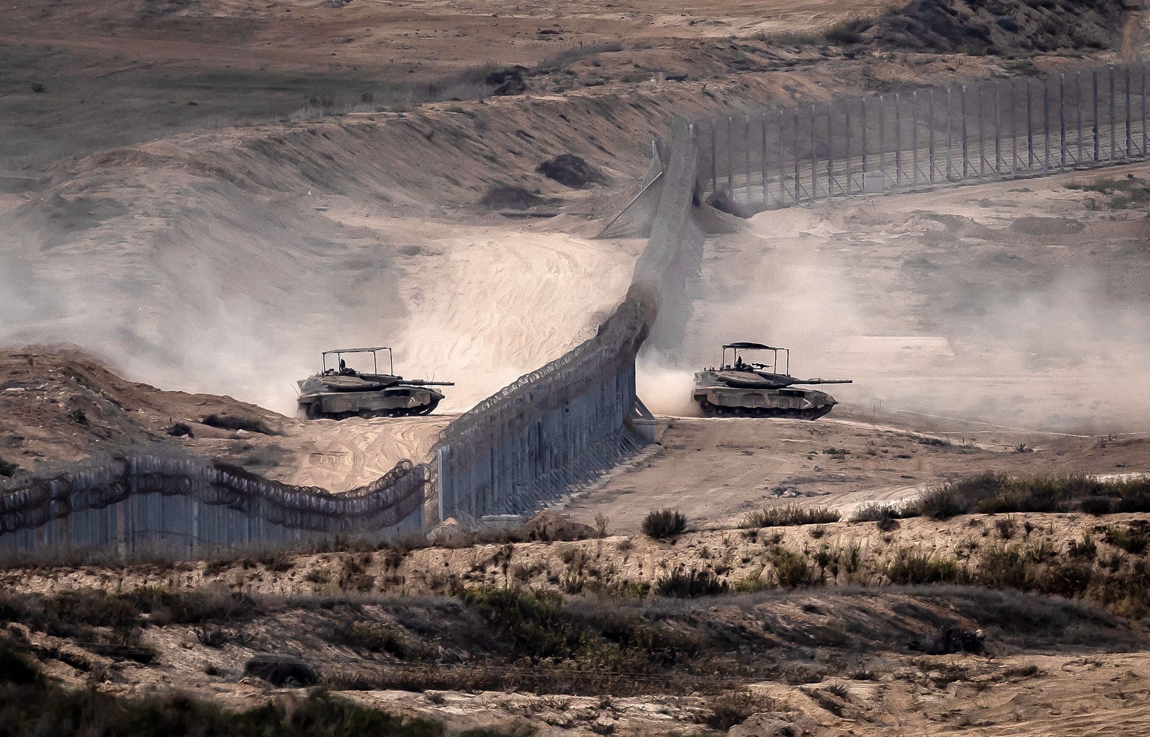 Israeli tanks cross a barbed wire fence at a position along the border with the Gaza Strip and southern Israel