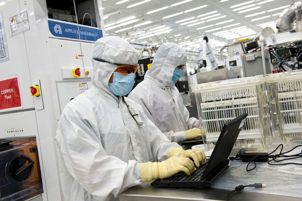 People in white work at a laboratory surrounded by equipment.