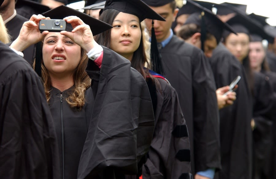Students in graduation regalia stand in line waiting for a ceremony.