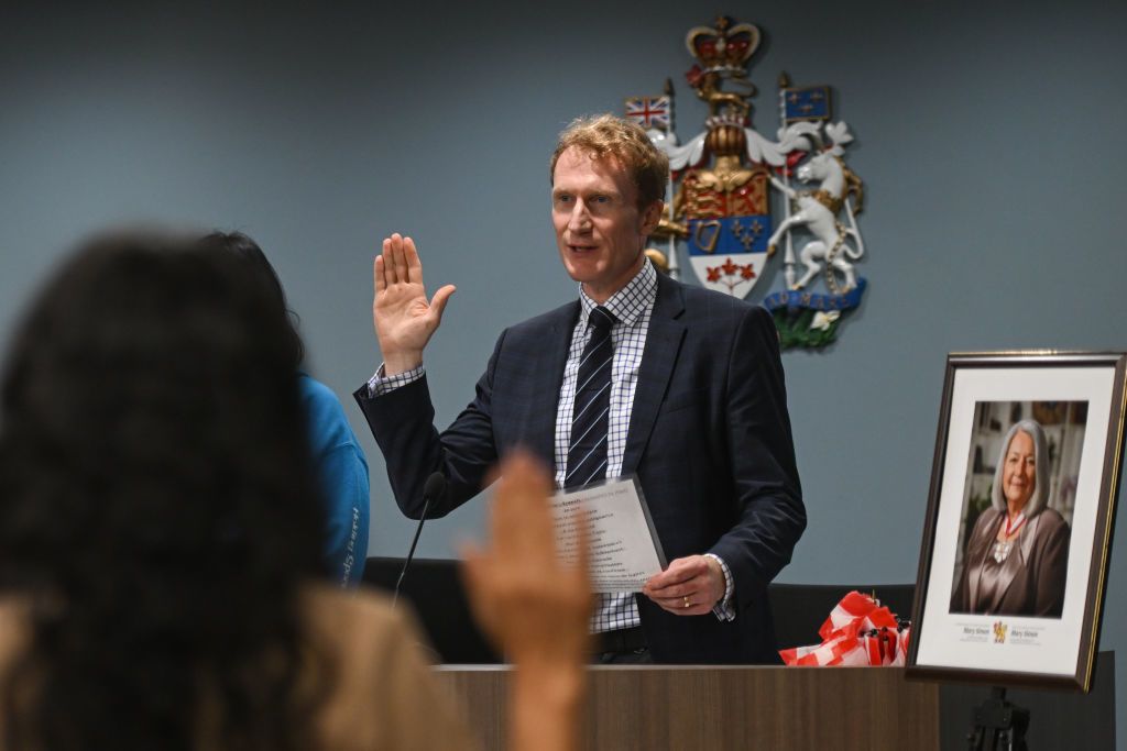 A man stands with his right hand raised as he recites an oath in front of a group.