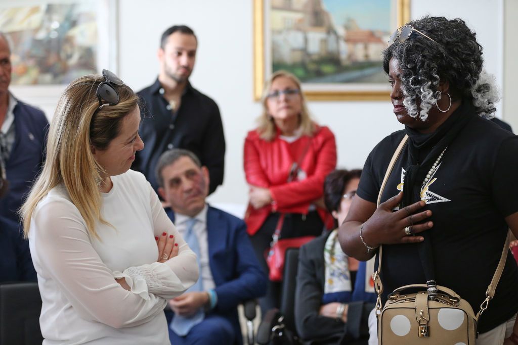 A blonde woman looks with crossed arms at a woman of African descent.