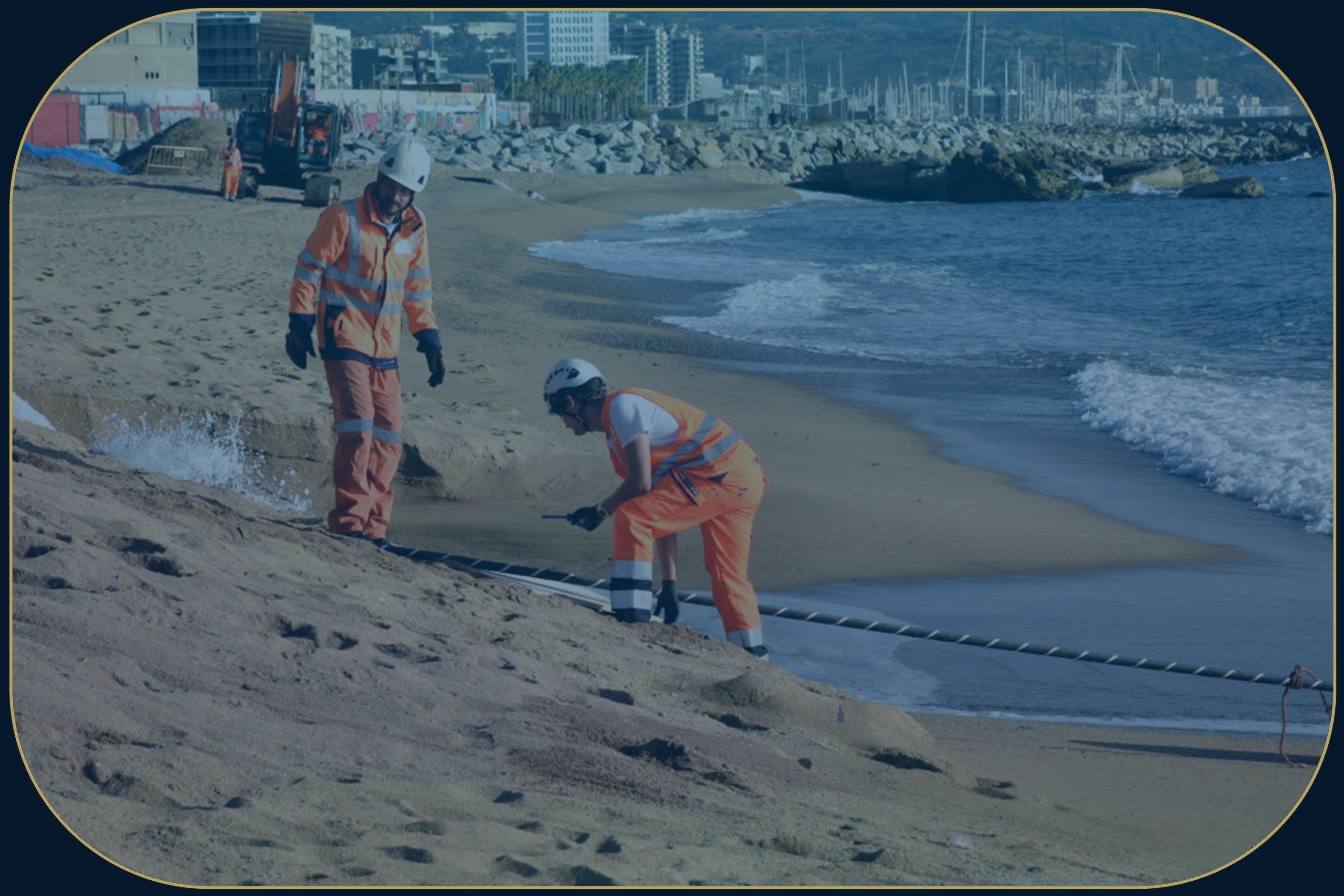 Two men with hard hats stand on a beach next to a striped cord.