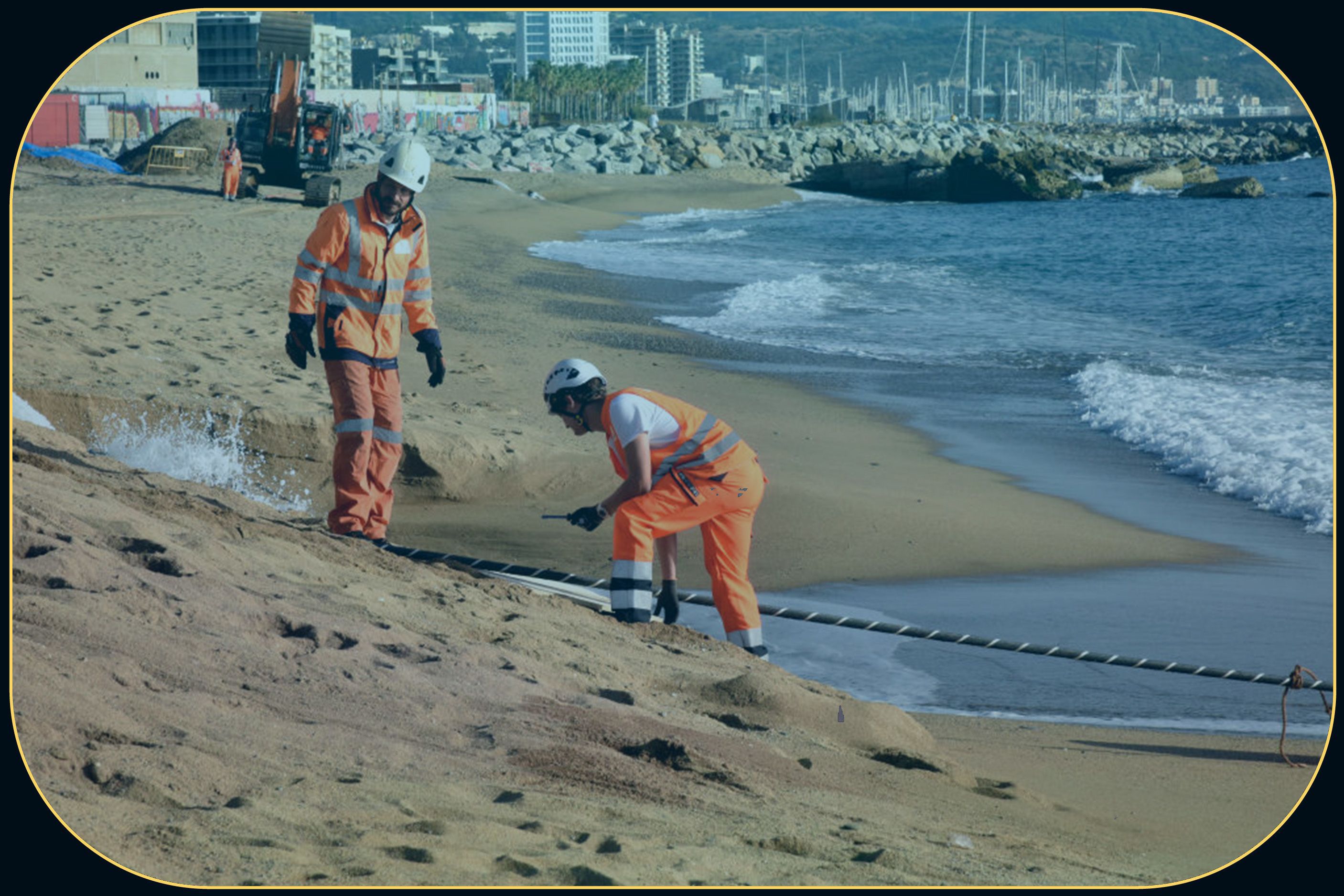 Two men with hard hats stand on a beach next to a striped cord.