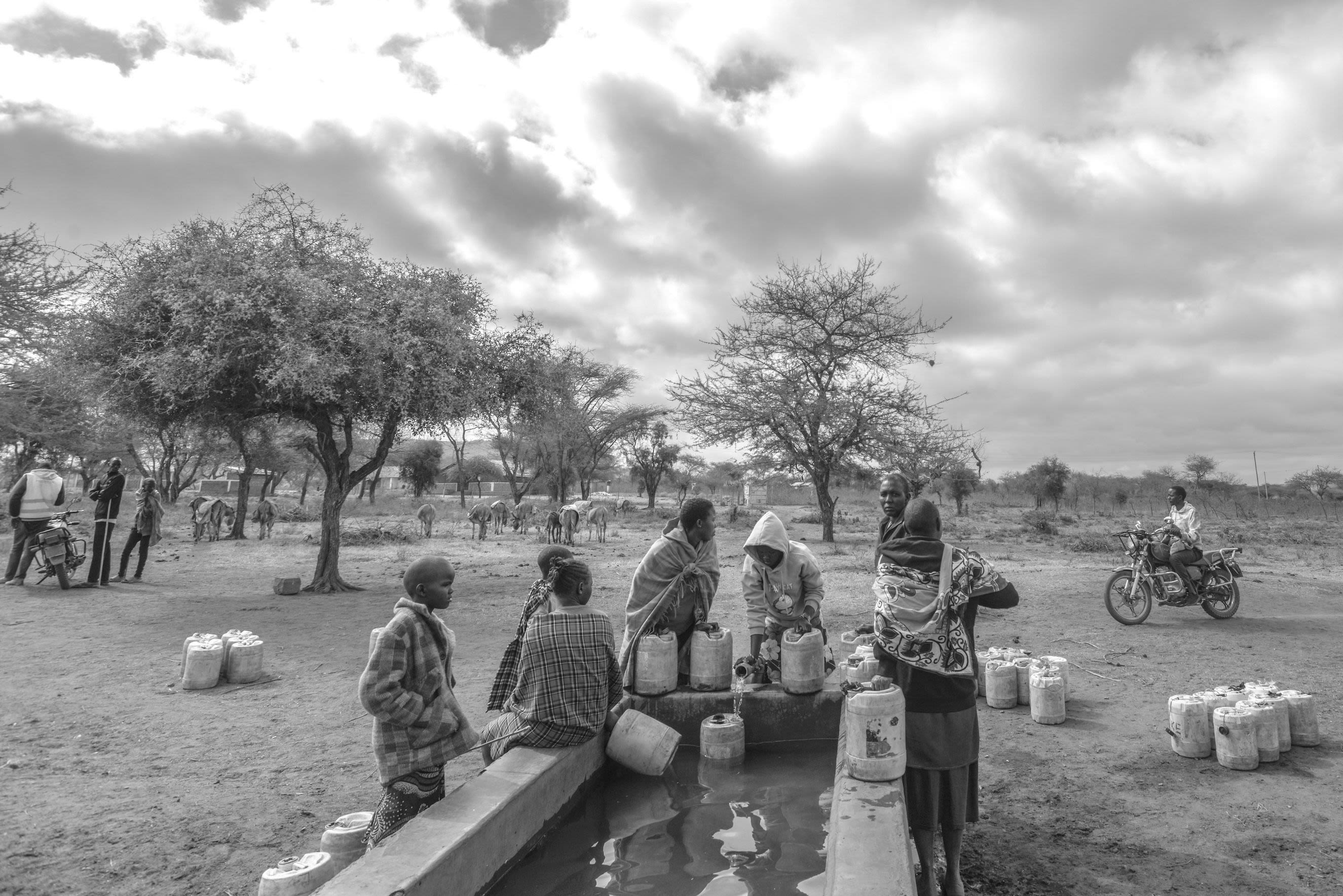 A group of young people gather around a well in a dry landscape.