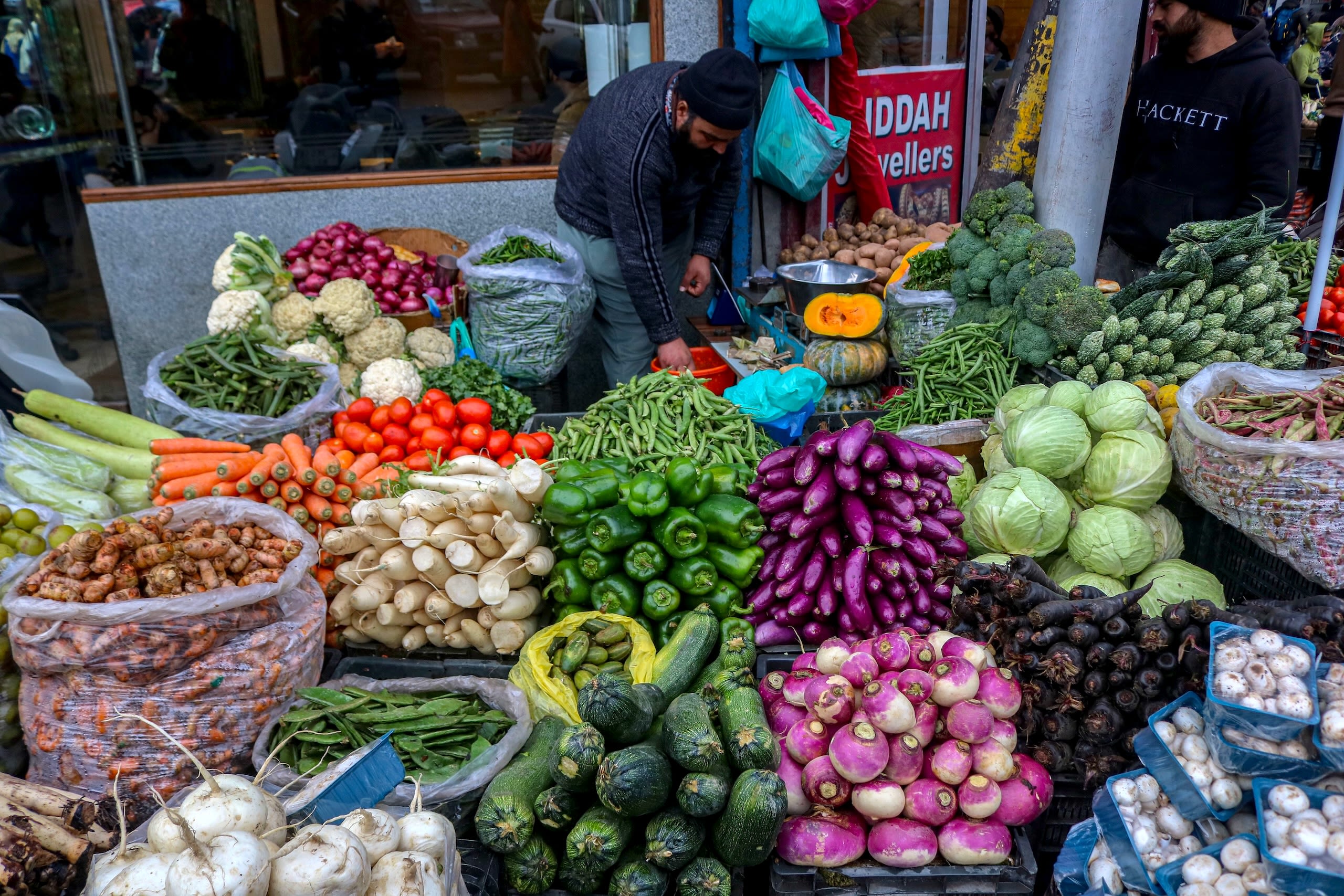 A man stands behind piles of colorful fruits and vegetables at a market.