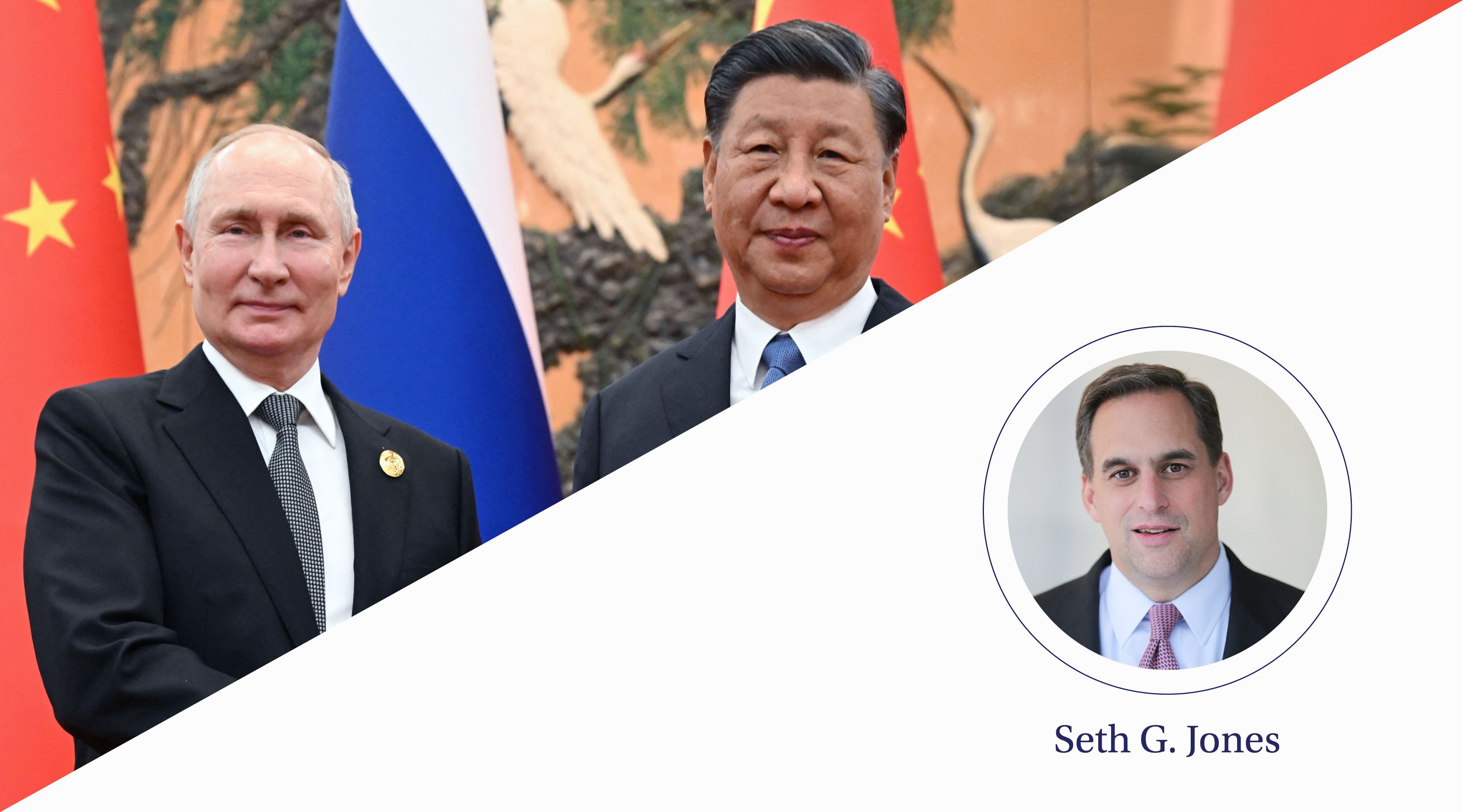 A short man with white hair stands next to a tall man as they shake hands in front of a row of flags.