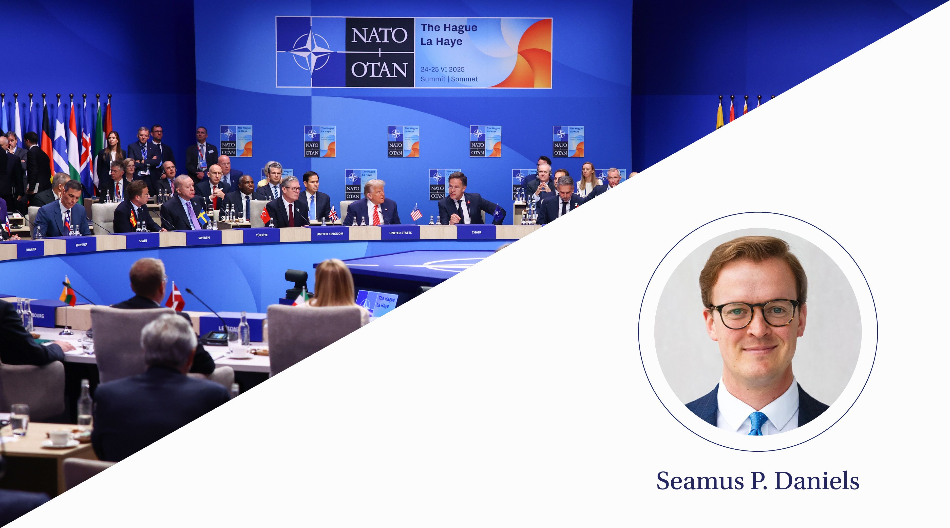 People sit around a circular table in a blue room with flags in the background.